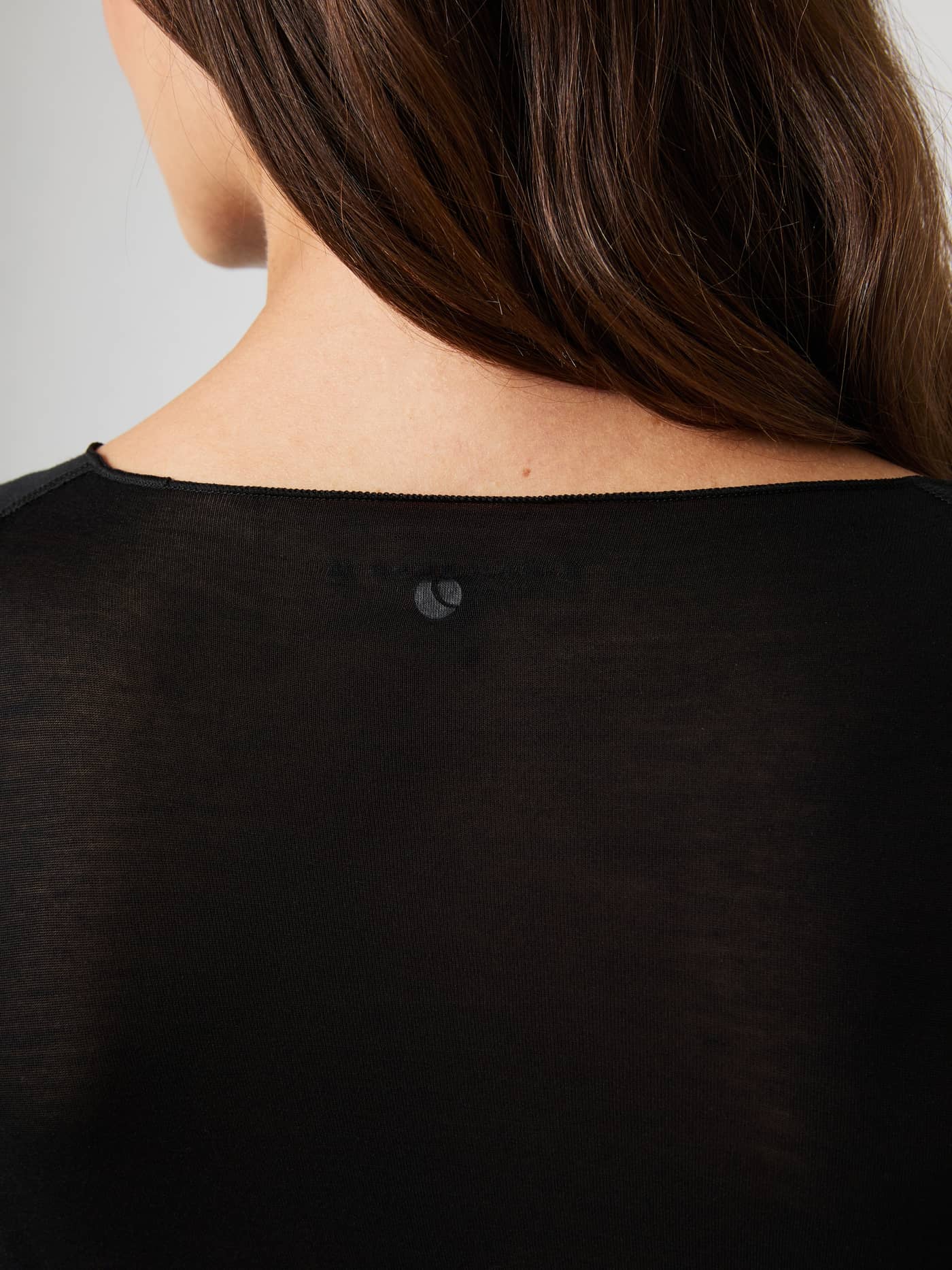 Close-up van de Studio Light Long Sleeve Top in Black Beauty (Zwart) met transparante stof en zwart logo voor training. - Image 5