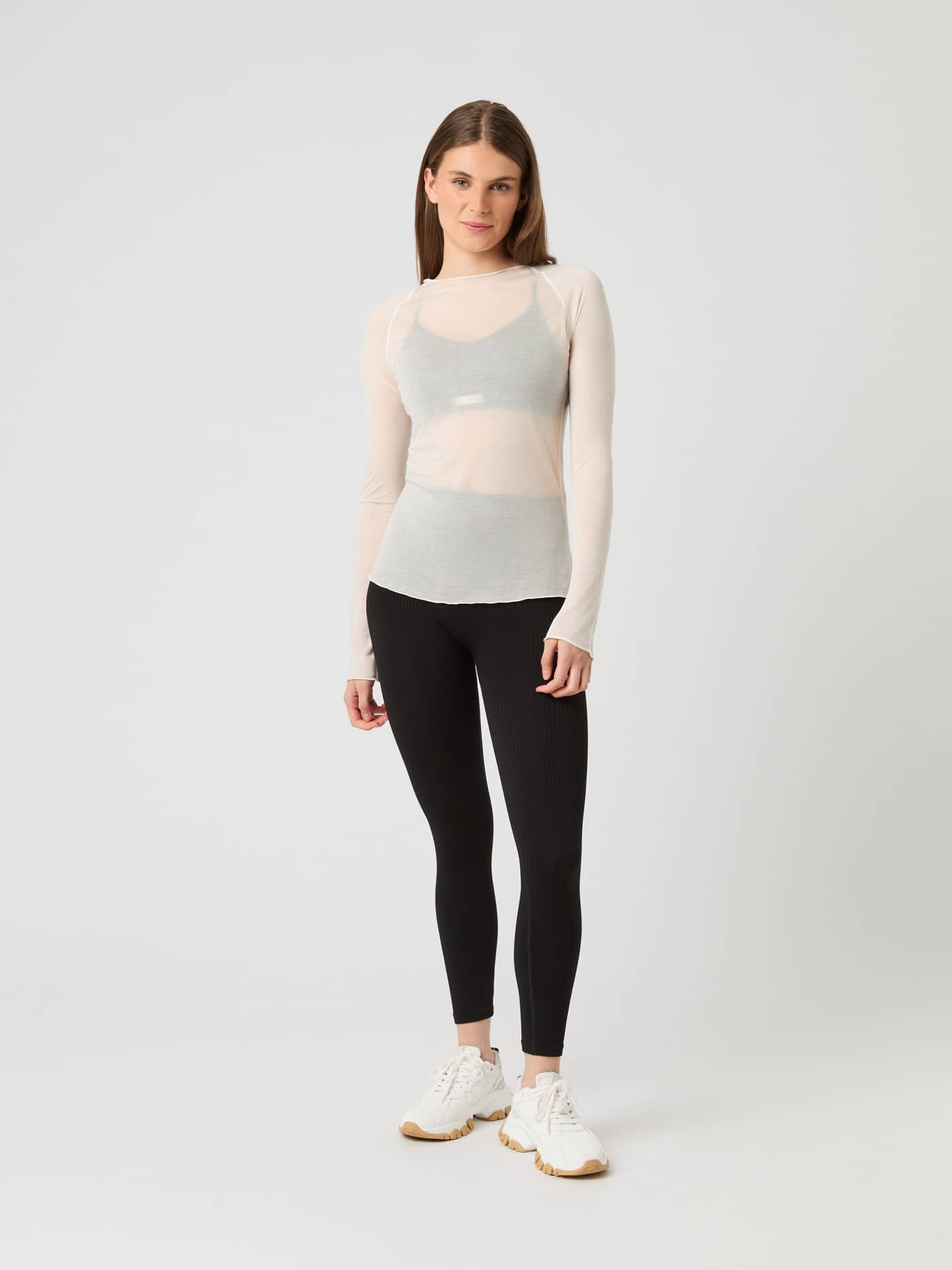 Front view of a model in the semi-transparent birch Studio Light Long Sleeve Top, paired with black leggings and sneakers. - Image 4