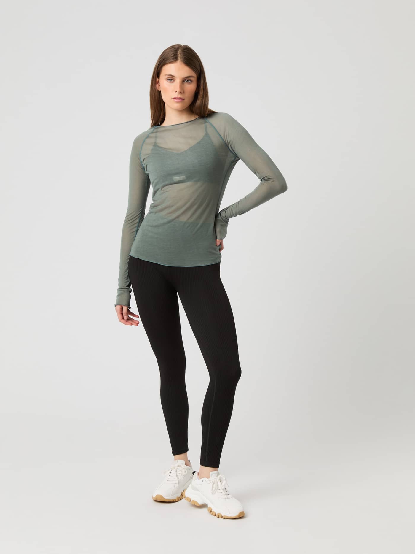 Full-length front view of a model in a green semi-transparent Björn Borg Studio Light Long Sleeve Top and black leggings. - Image 4