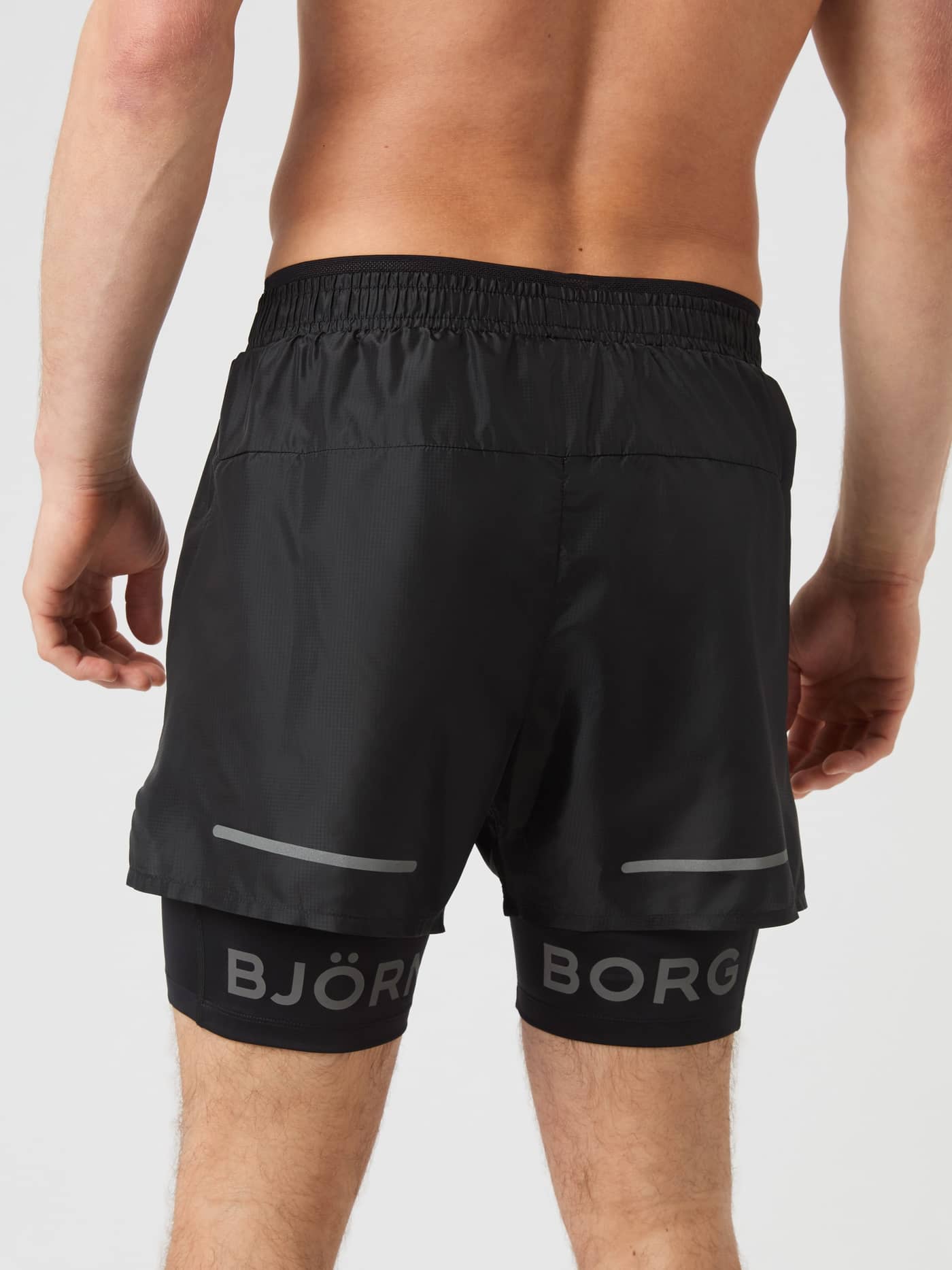 Back view of a man wearing the functional Borg Running Shorts 2 In 1 in Black Beauty (Black) with grey reflective logos. - Image 2
