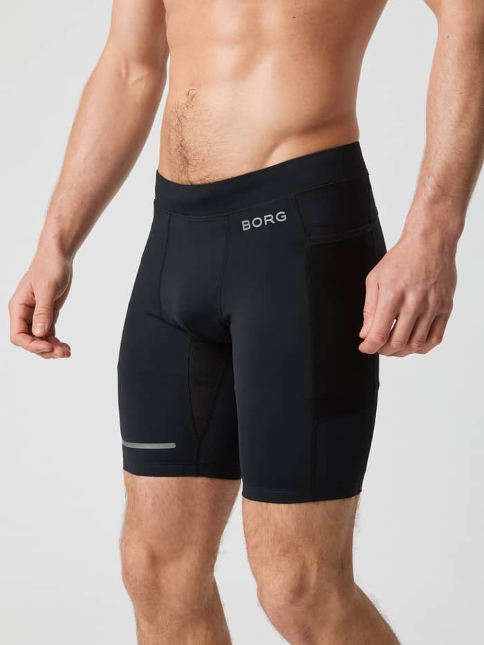 Zijaanzicht van een man in de Borg Running Short Tights in Black Beauty (Zwart) met mesh zakken en een zilveren logo.