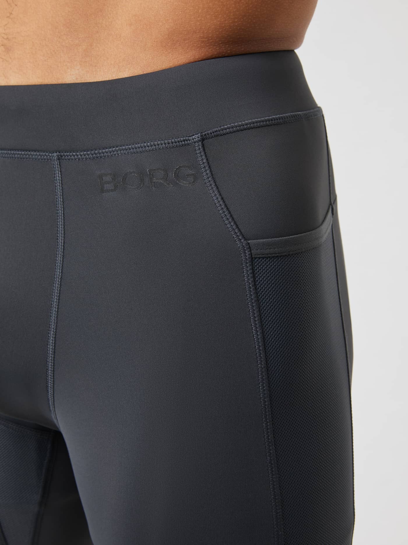 Detailed close-up of the Borg Running Short Tights in Asphalt (Grey) showing a mesh pocket and tone-on-tone logo. - Image 5