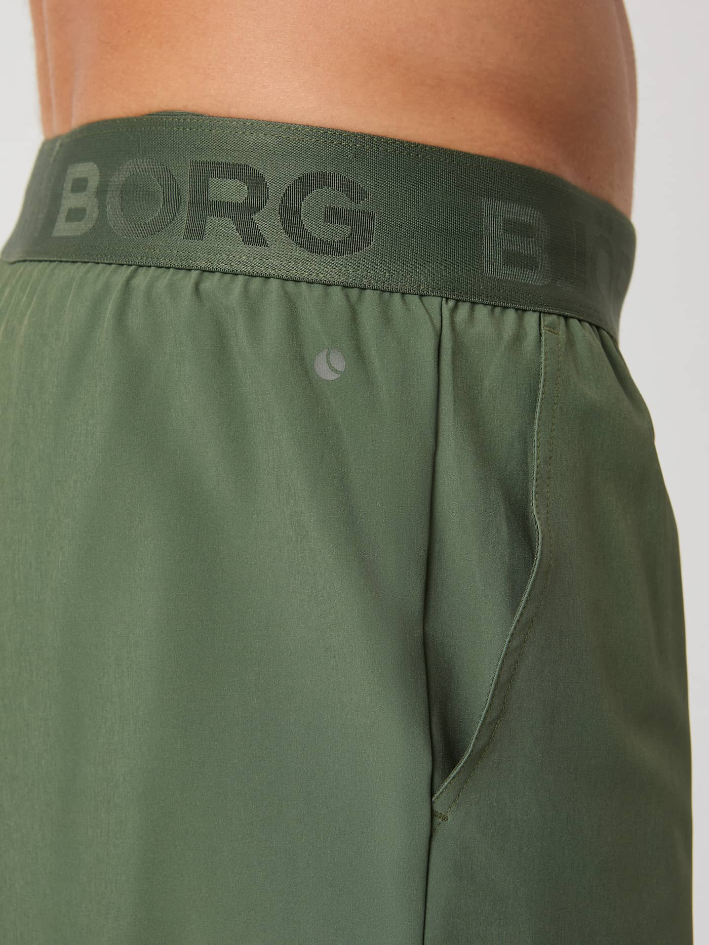 Close-up of the Borg 9" Shorts in thyme green, detailing the iconic Borg logo on the elastic waistband and the side pocket. - Image 4