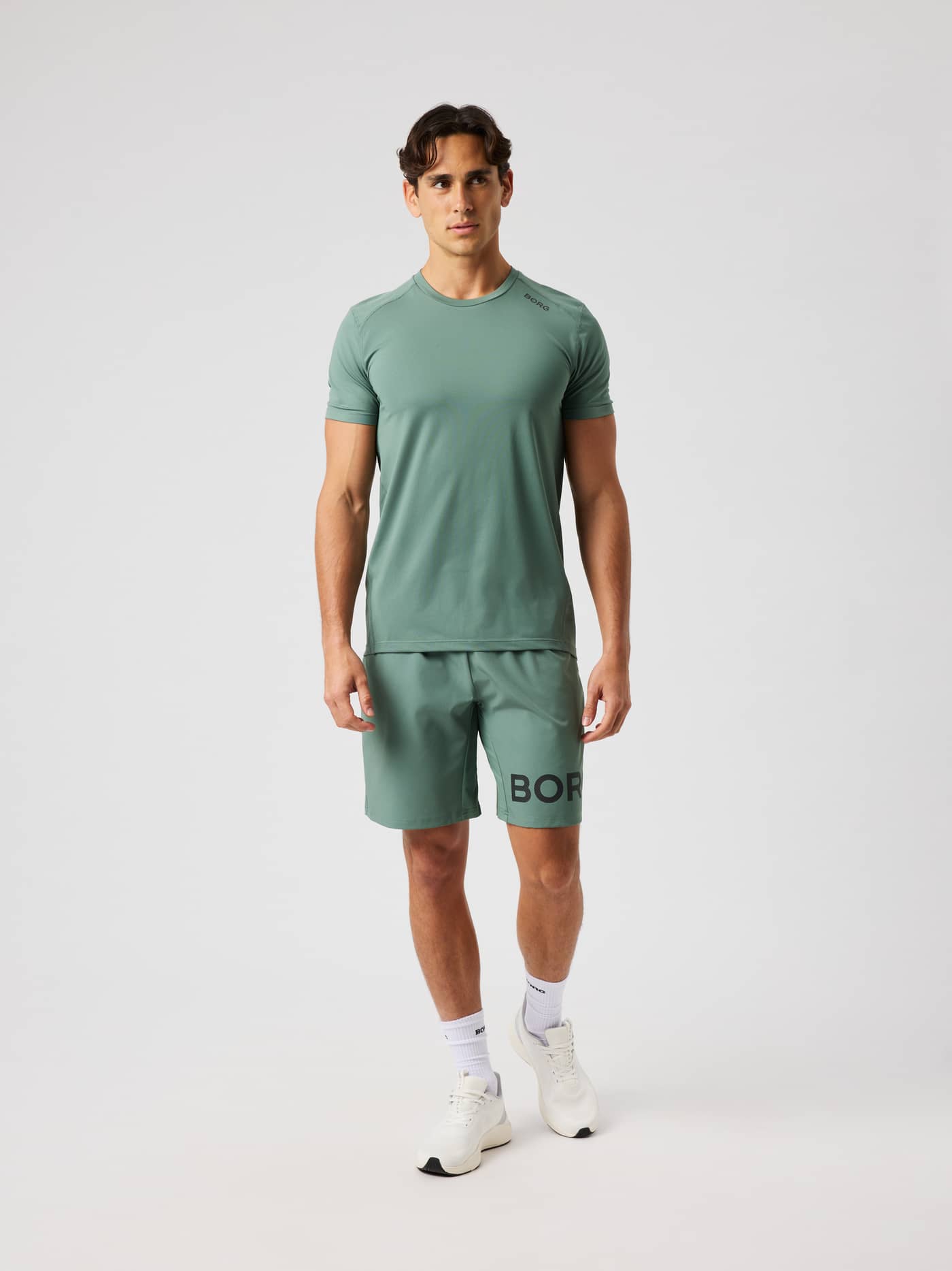 Male model wearing the Borg Shorts 9 Inch in Laurel Wreath (green) with training t-shirt and white sneakers. - Image 3
