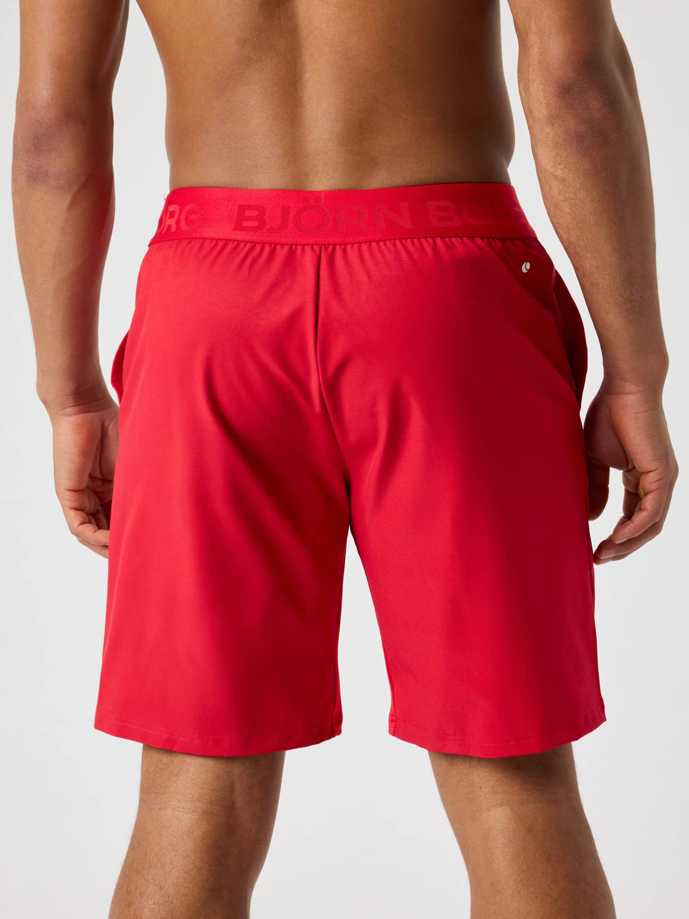 Back view of a man wearing Lychee (Red) Björn Borg Shorts 9 Inch with a red logo waistband for training and tennis. - Image 2