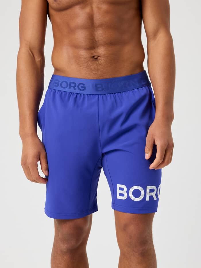 Vorderansicht eines Mannes in Clematis Blue (Blau) Borg Shorts 9 Inch mit weißem perforiertem Logo zum Training.