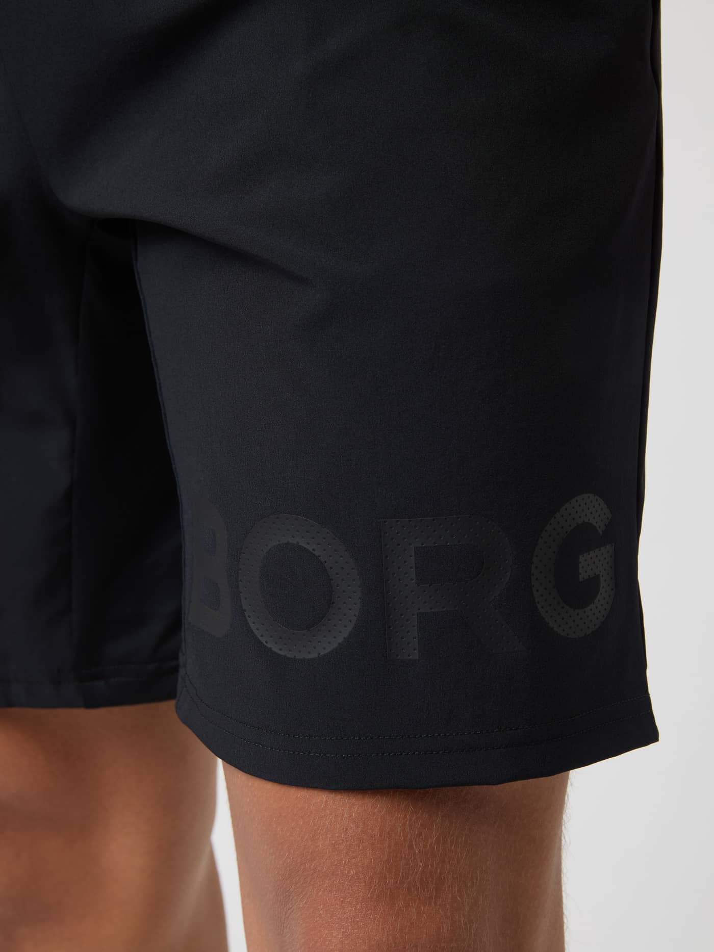 Närbild på det stora perforerade logotrycket på benet av Borg Shorts 9 Inch i Black Tonal Logo (Svart) för träning. - Image 5