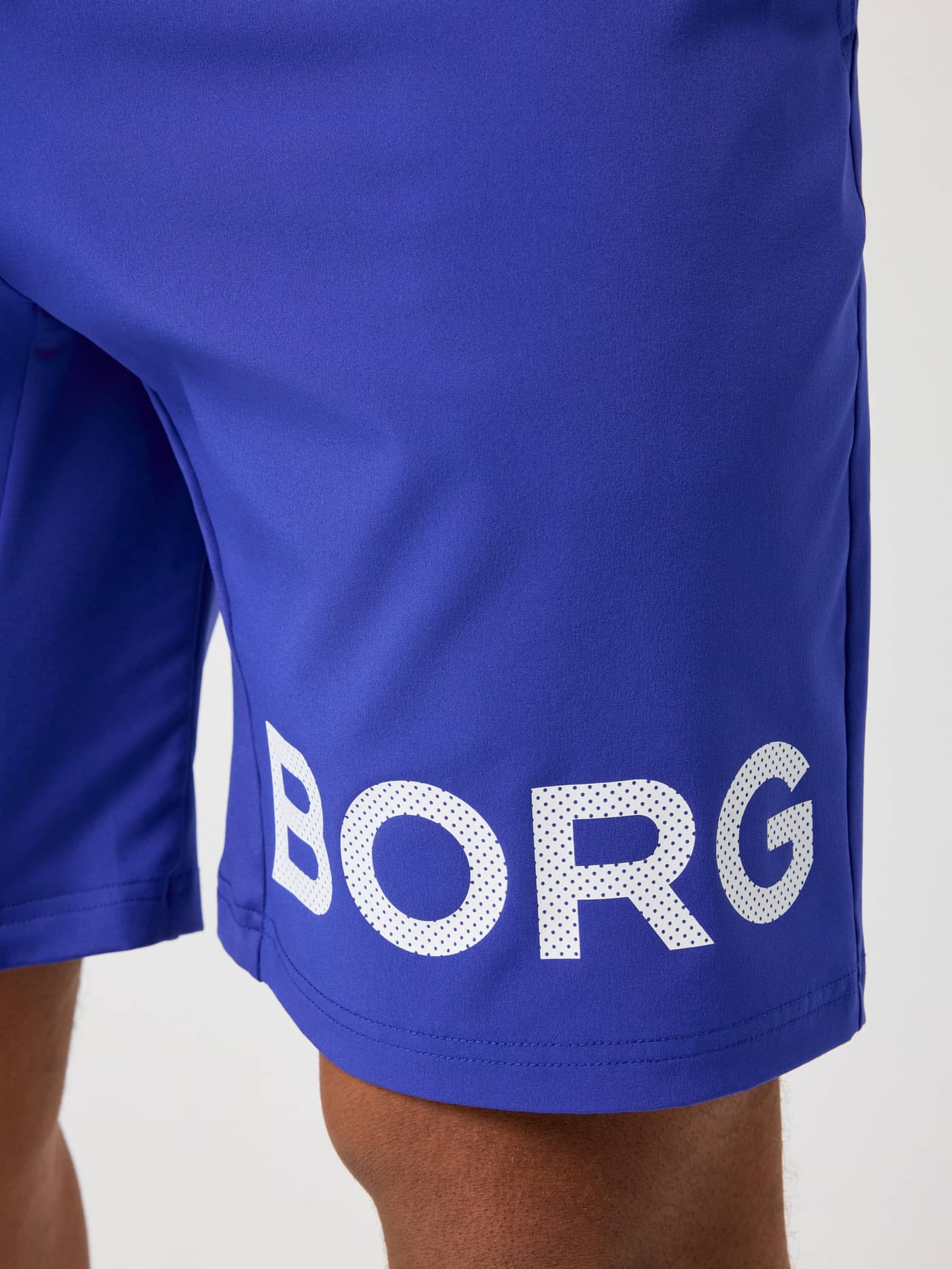 Close-up of the white perforated logo on the Clematis Blue (Blue) Borg Shorts 9 Inch, designed for men's training. - Image 6