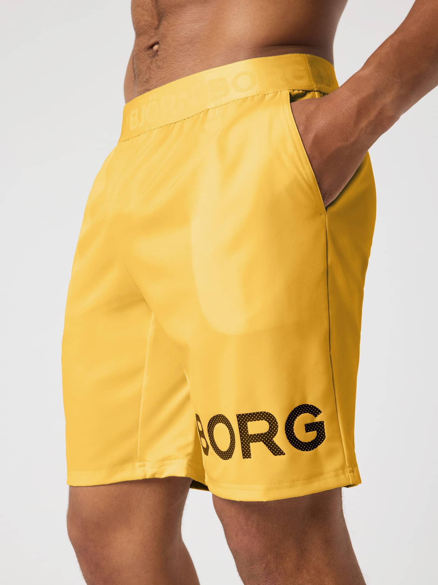 Close-up of Borg Shorts 9 Inch in Citrus (Orange) for training, featuring a black perforated logo and side pockets. - Image 3
