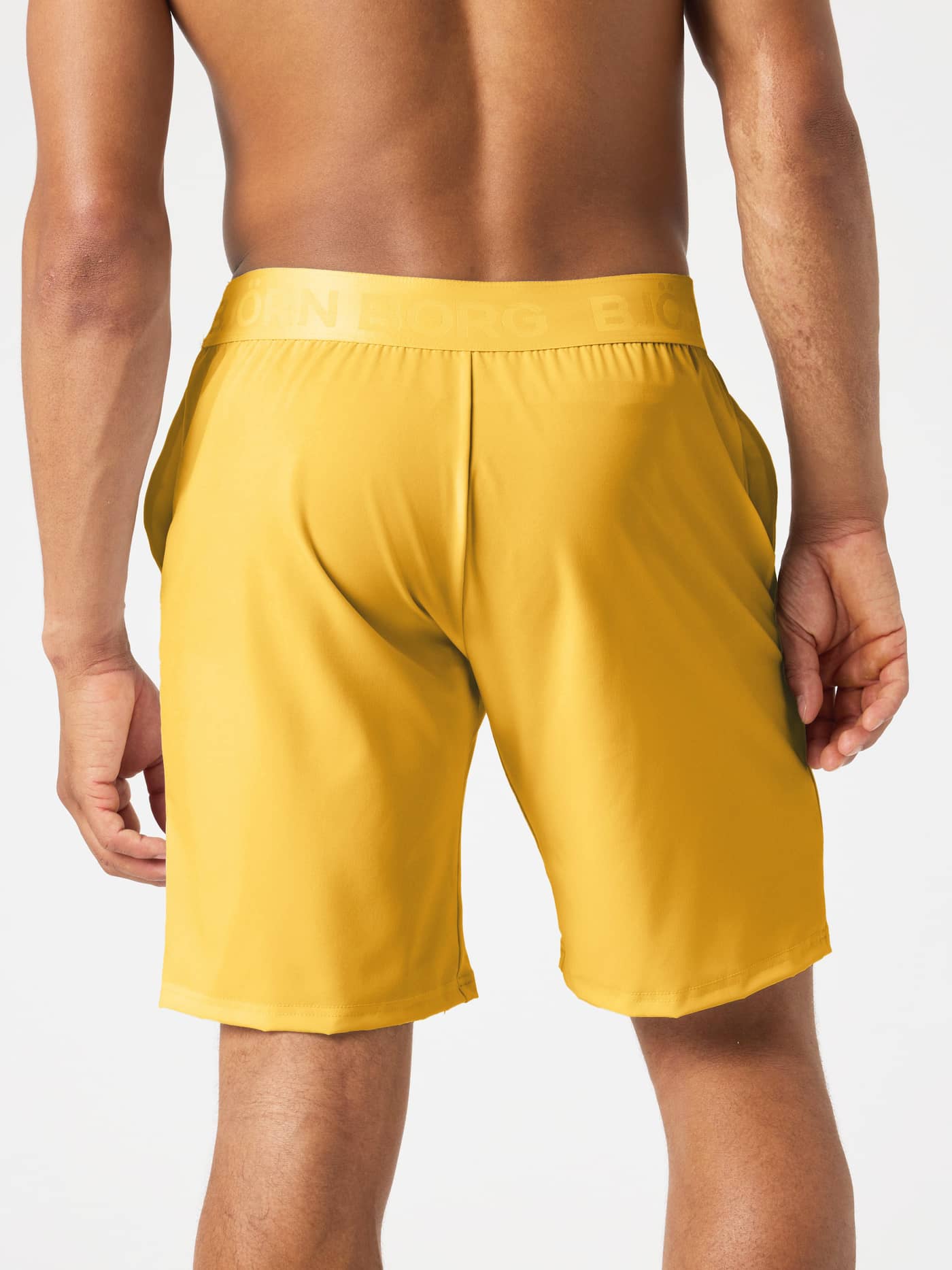 Back view of a man wearing Borg Shorts 9 Inch in Citrus (Orange) featuring a branded waistband for training sessions. - Image 2