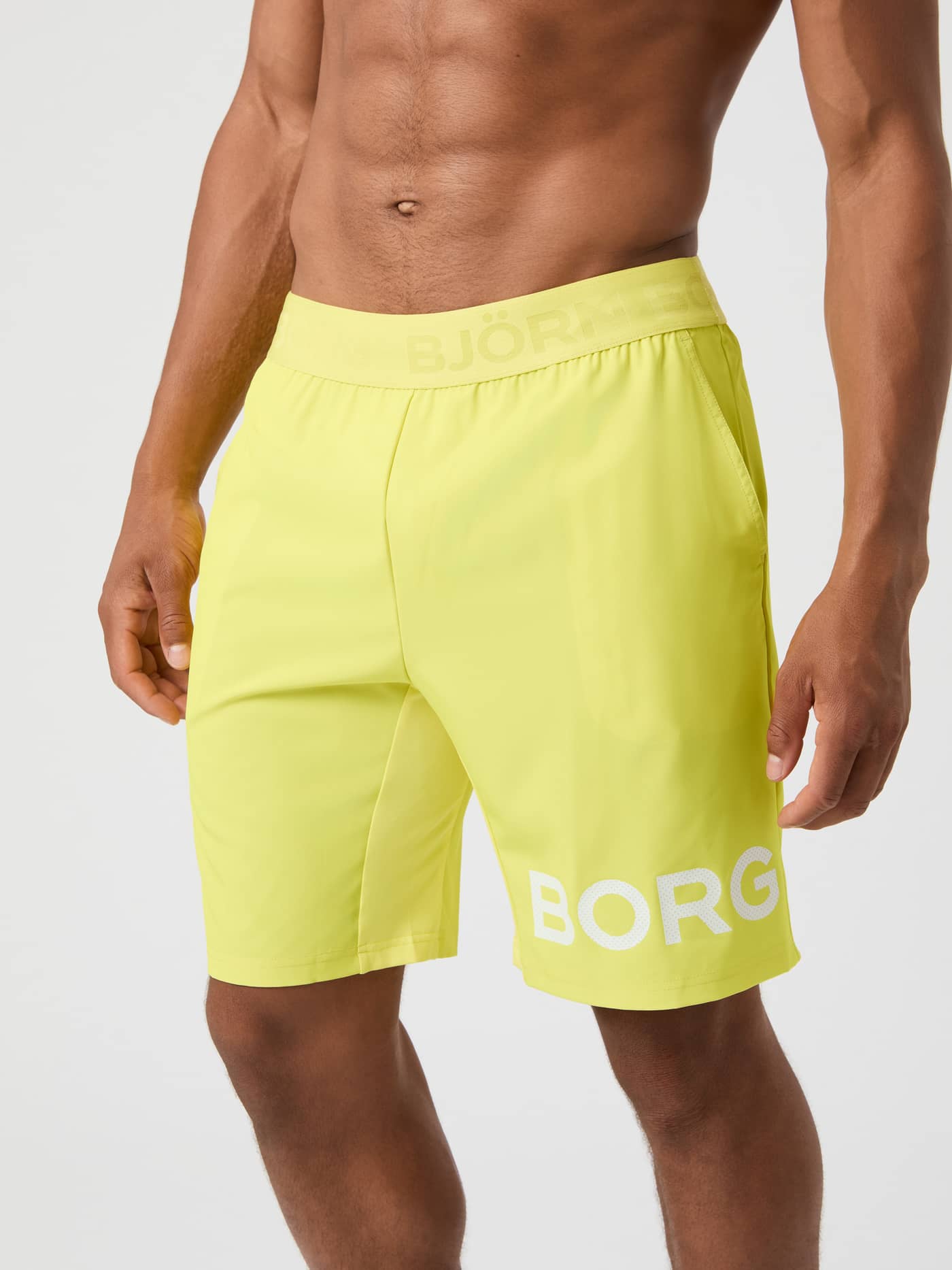 Side view of a man wearing the bright yellow Björn Borg 9-inch Borg Shorts against a white background. - Image 1