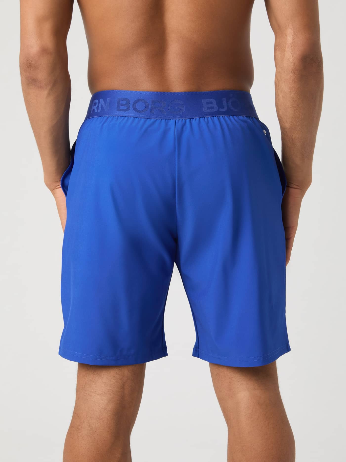Vista posterior de un modelo con los Borg Shorts 9 Inch en Surf The Web (Azul) y cintura elástica con logo de entrenamiento. - Image 2