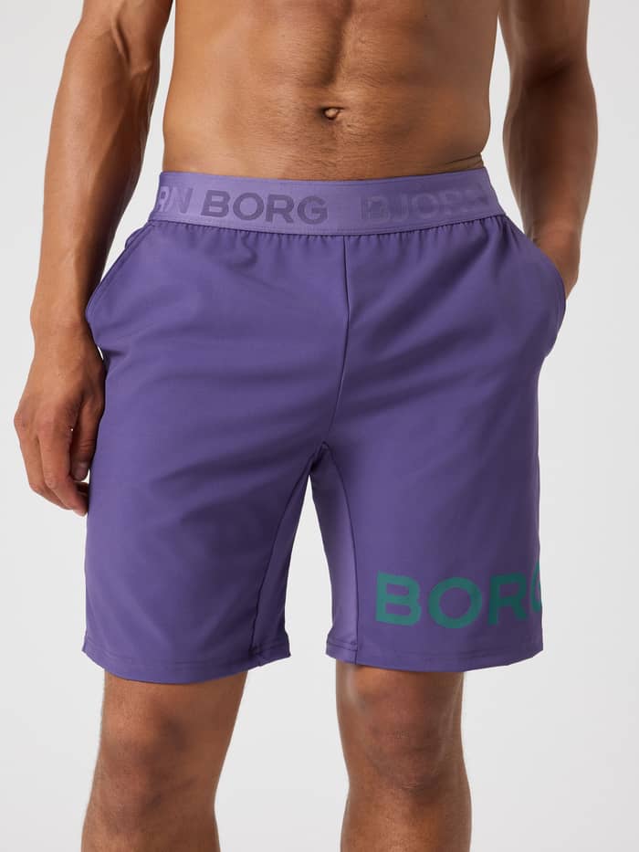 Vooraanzicht van een man in de Borg Shorts 9 Inch in Mystical (Paars) met groen logo, ideaal voor training en stijl.