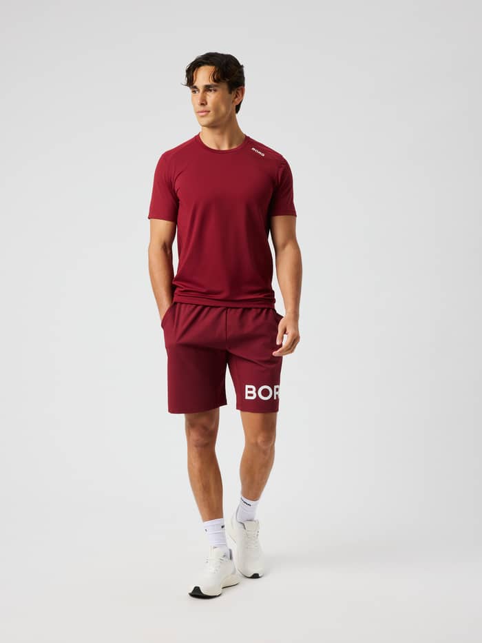 Man wearing Borg Shorts 9 Inch in cabernet (red) with a perforated logo print for training.