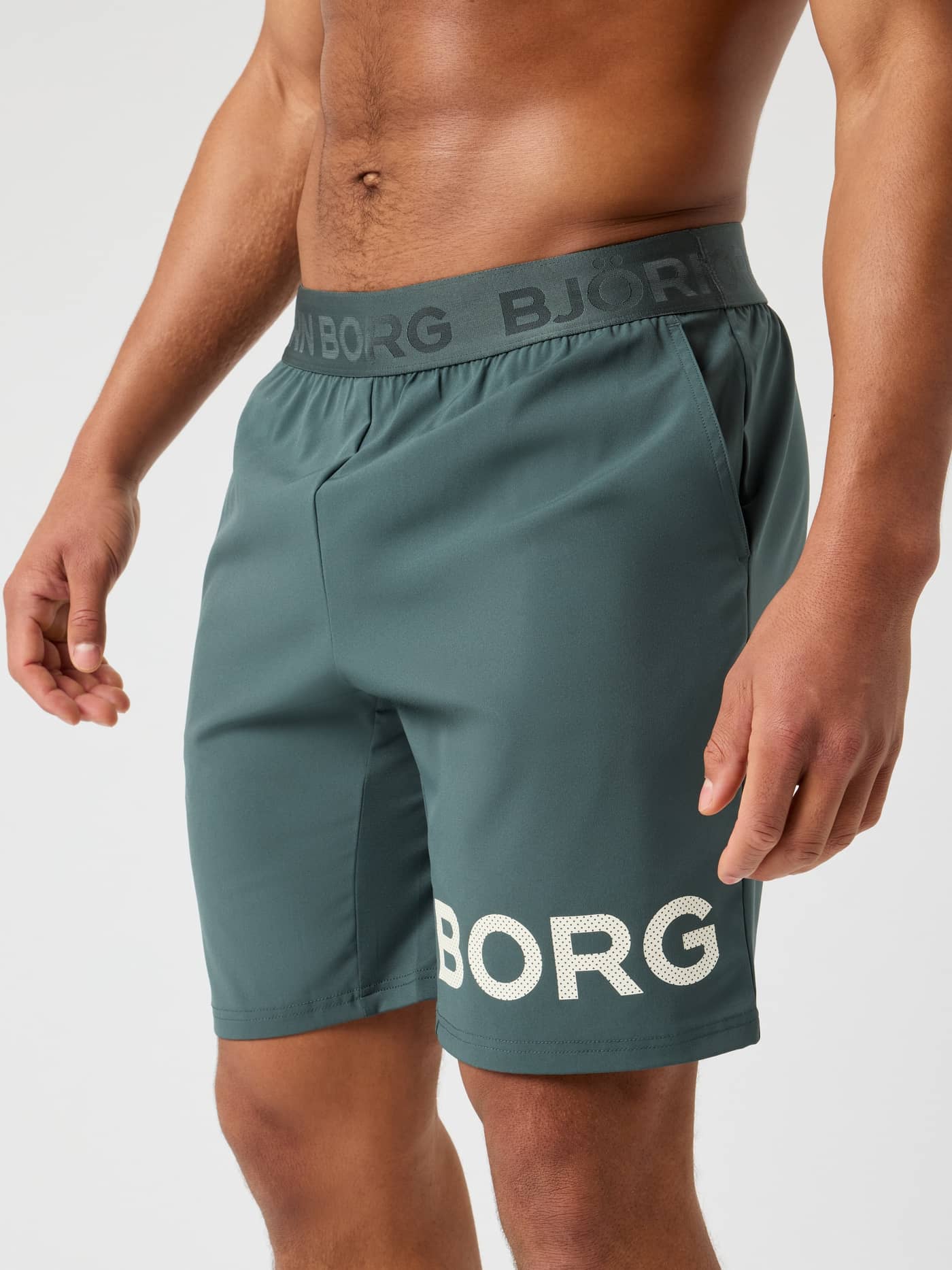 Front view of a man wearing Urban Chic (Green) Borg Shorts 9 Inch for training, featuring a perforated white logo. - Image 1