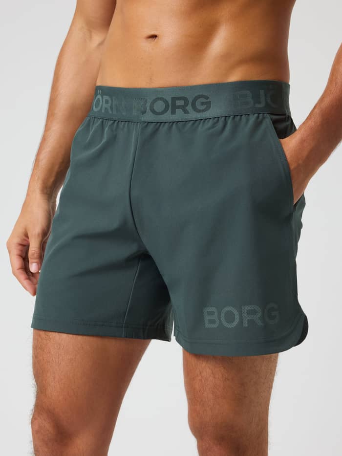 Front view of a man wearing the training Borg Shorts 6 Inch in Urban Chic (Green) with a tonal logo waistband.