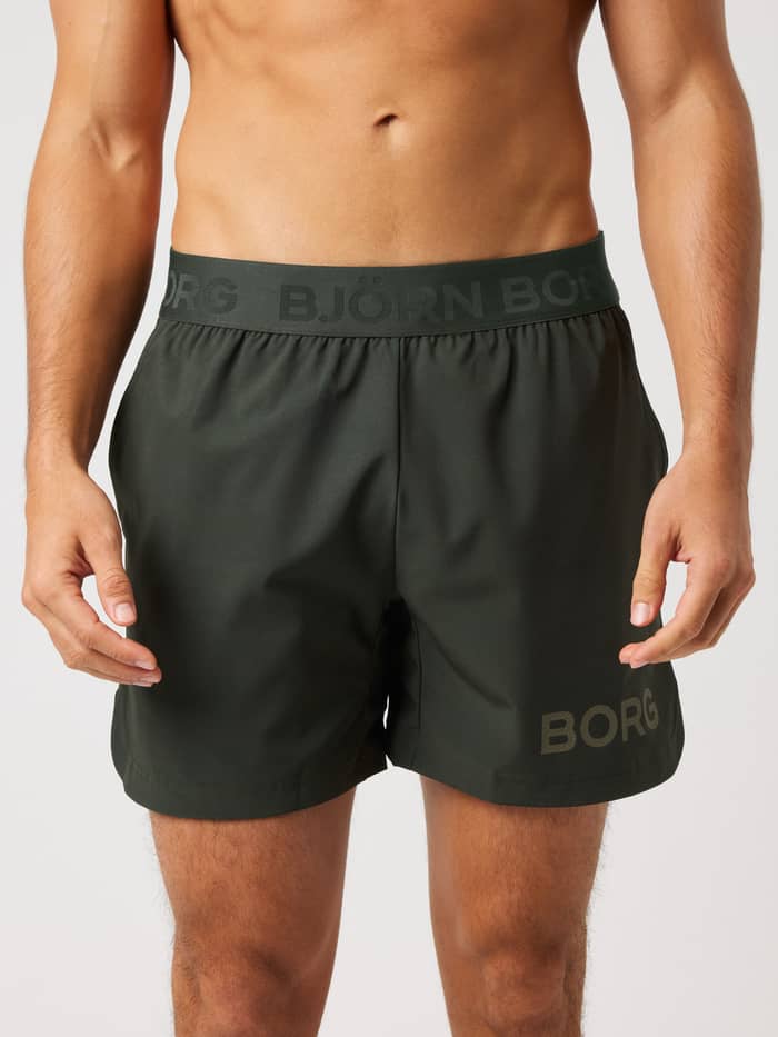 Front view of a man wearing Borg Shorts 6 Inch in Rosin (Green) for training, with technical side slits and a green logo.