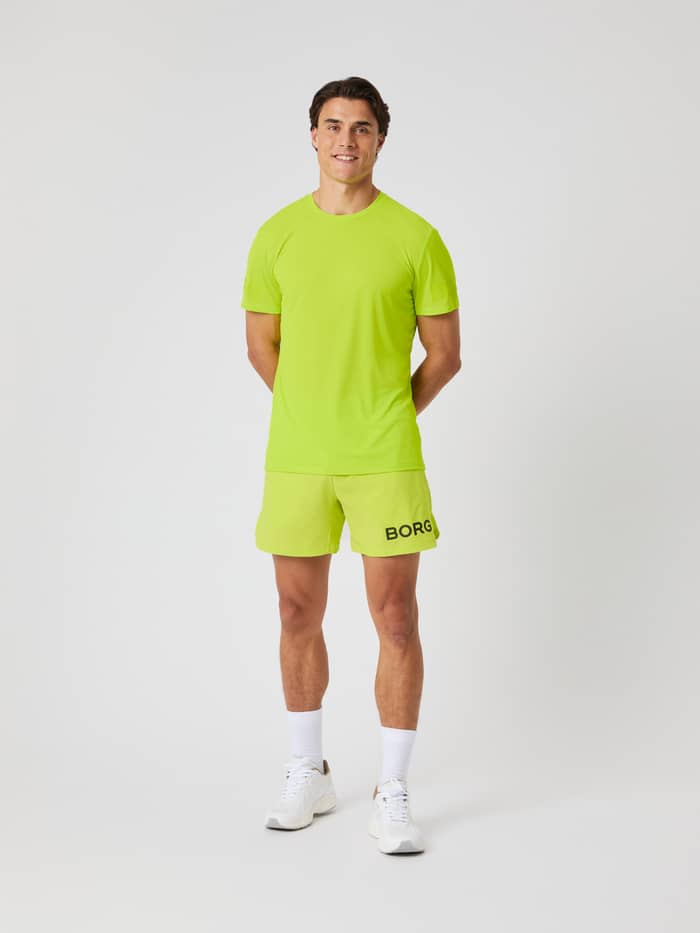 Vooraanzicht van een man in de Borg Shorts 6 Inch in Acid Lime (Groen) met zwart logo en bijpassend shirt voor training. - Image 2