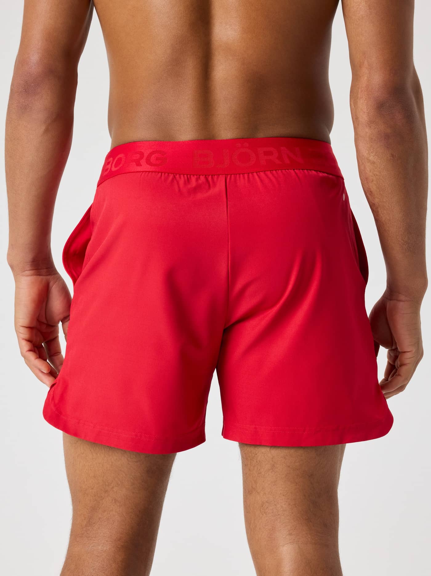 Back view of a man wearing the Lychee (Red) Borg Shorts 6 Inch with a tonal branded waistband for tennis and training. - Image 2