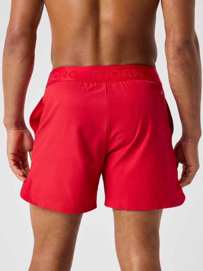 Back view of a man wearing the Lychee (Red) Borg Shorts 6 Inch with a tonal branded waistband for tennis and training. - Image 2