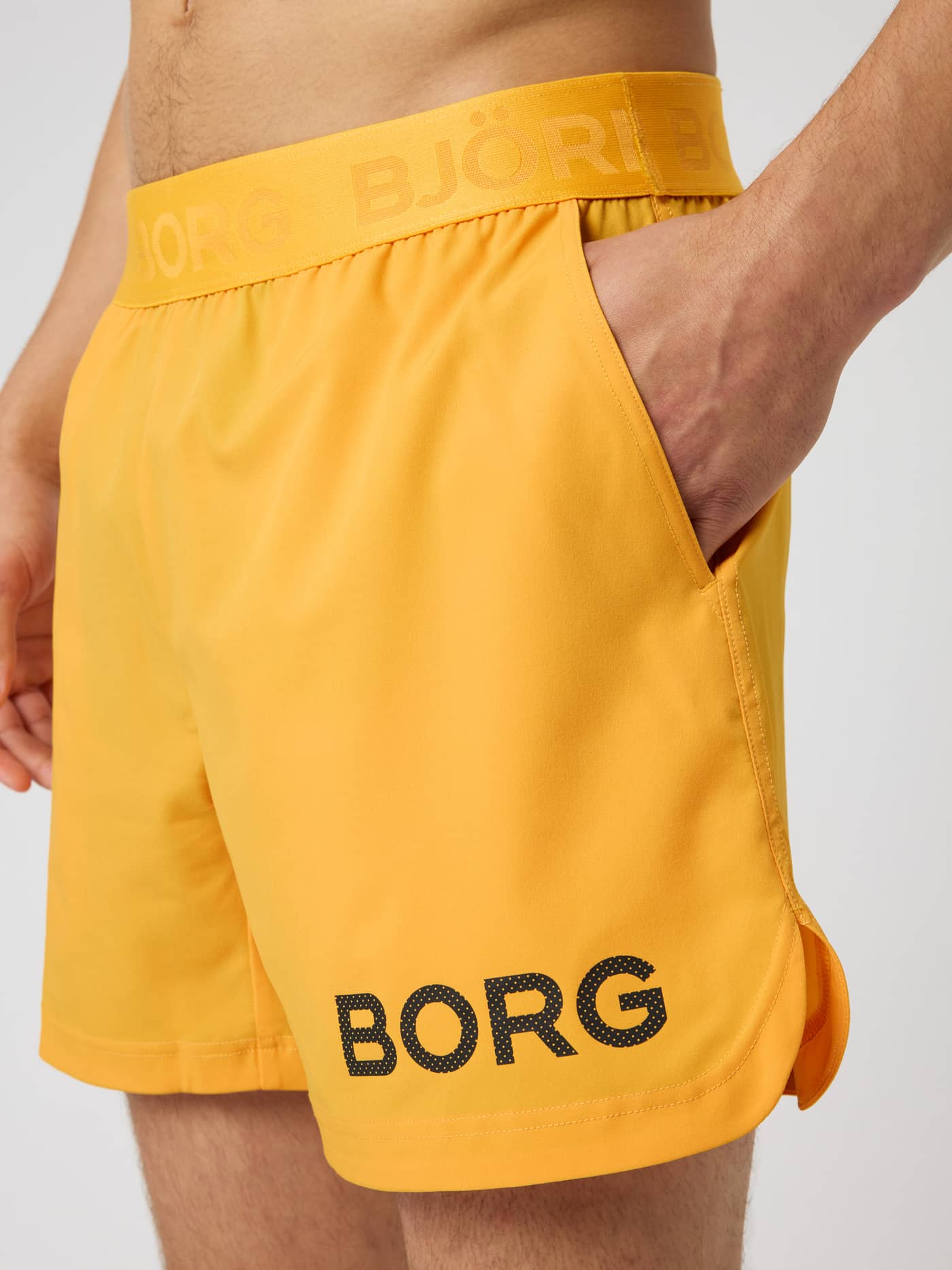 Close-up of the Borg Shorts 6 Inch in Citrus (Orange) featuring a black perforated logo and side pocket for training. - Image 5