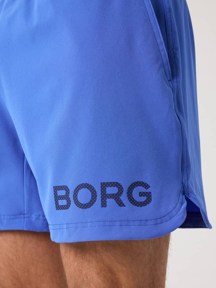 Close-up van de Borg Shorts 6 Inch in Amparo Blue (Blauw) met een donkerblauw logo en zijsplit voor training. - Image 5