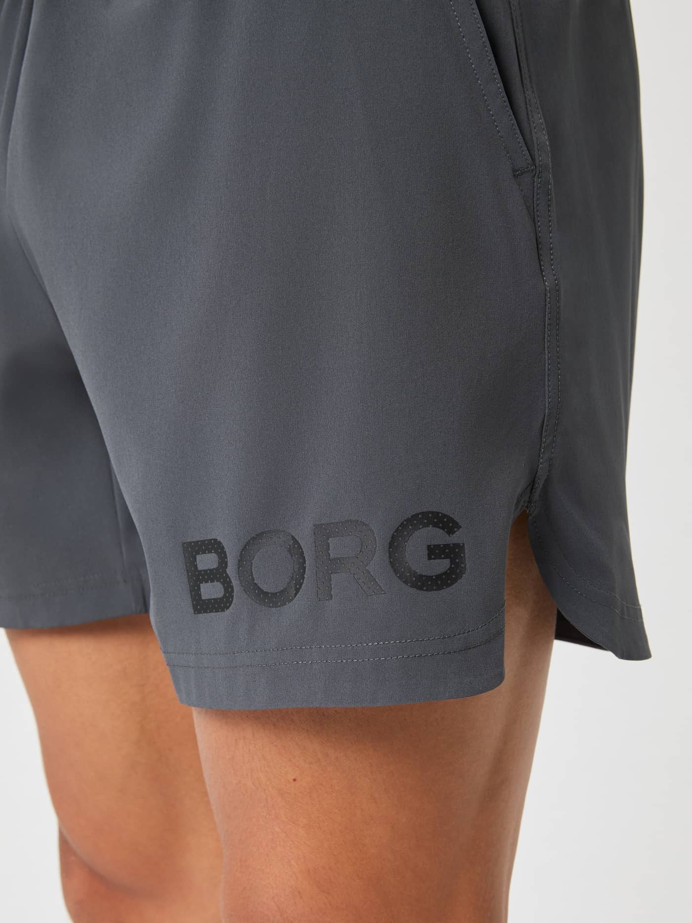 Close-up side view of a model's thigh wearing the Asphalt Borg 6" Shorts, detailing the BORG logo and side slit. - Image 4