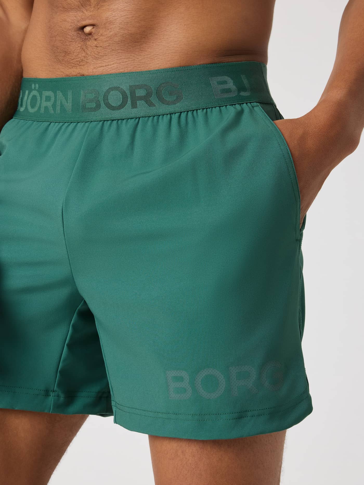 Close-up of a man wearing Mallard Green (Green) Borg Shorts 6 Inch, highlighting the logo waistband and training style. - Image 6