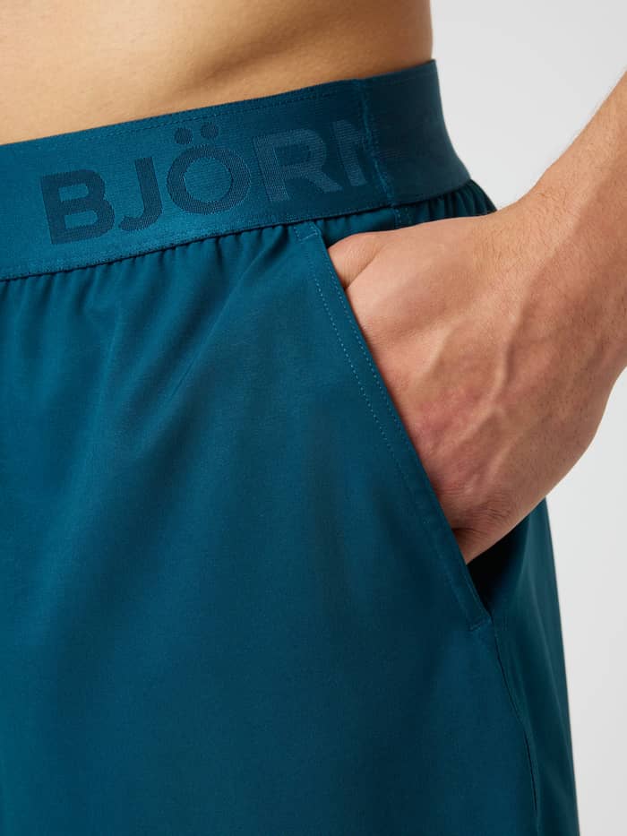 Gros plan du Borg Shorts 6 Inch Reflecting Pond (Bleu) avec poche latérale et taille élastique à logo bleu de training. - Image 5