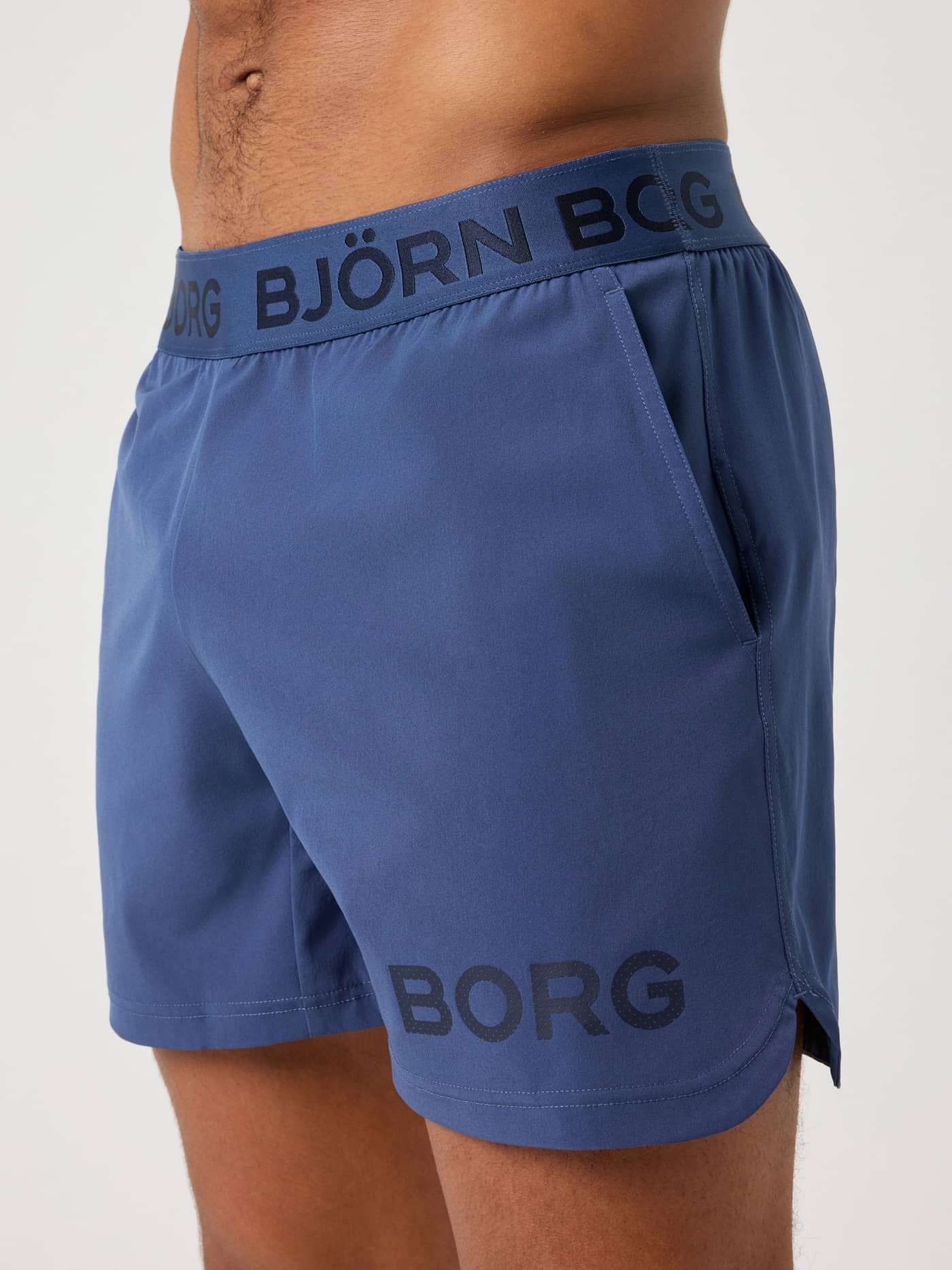 Close-up side view of a man wearing blue Borg 6-inch Shorts, highlighting the branded waistband, side pocket and leg logo. - Image 4