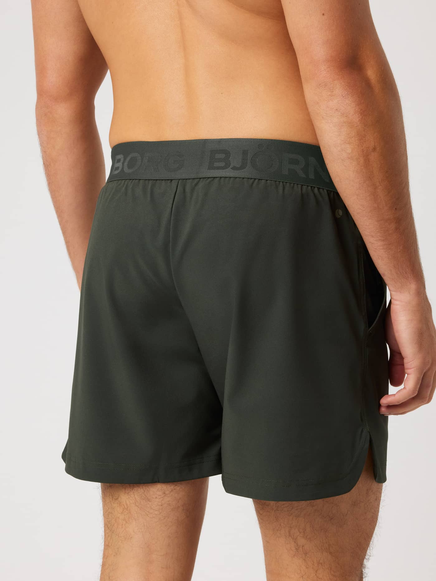 Back view of a man in Borg Shorts 6 Inch in Rosin (Green) for training, featuring a tonal logo waistband and side slits. - Image 2