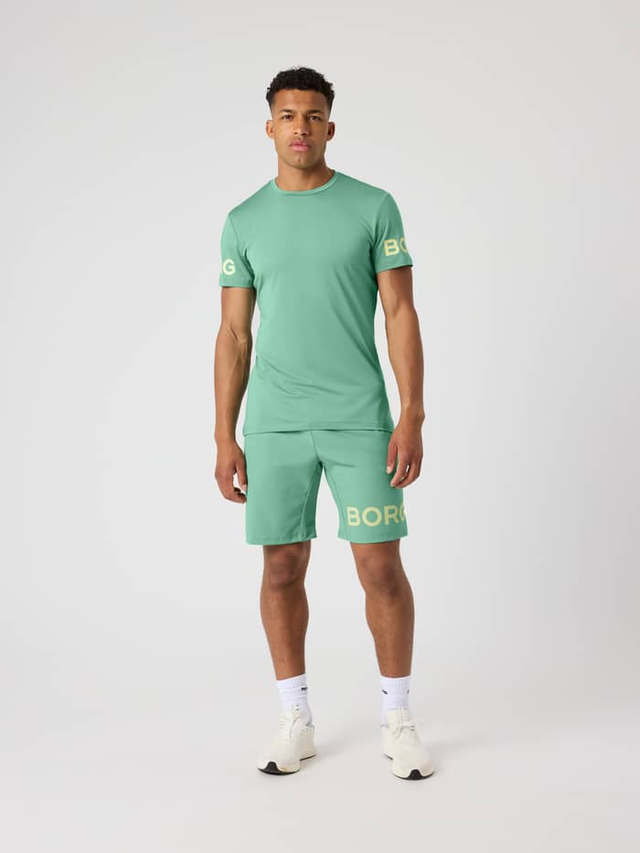 Borg T-Shirt i Malachite Green (Grøn) set forfra i fuld figur med et gult logo til funktionel træning. - Image 4