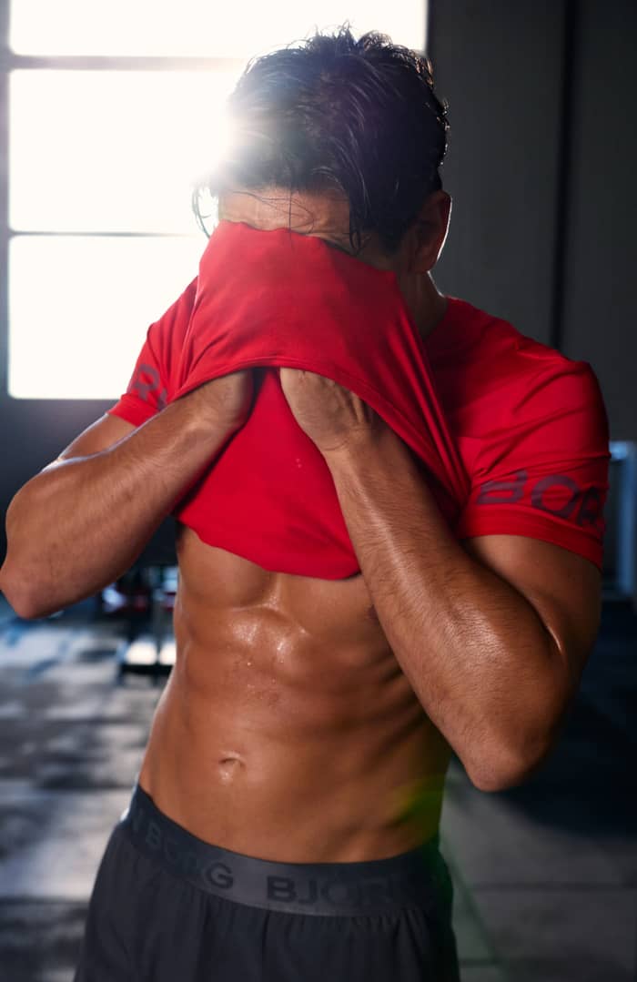 Close-up of a man wiping sweat with the Borg T-Shirt in Flame Scarlet (red) during training.