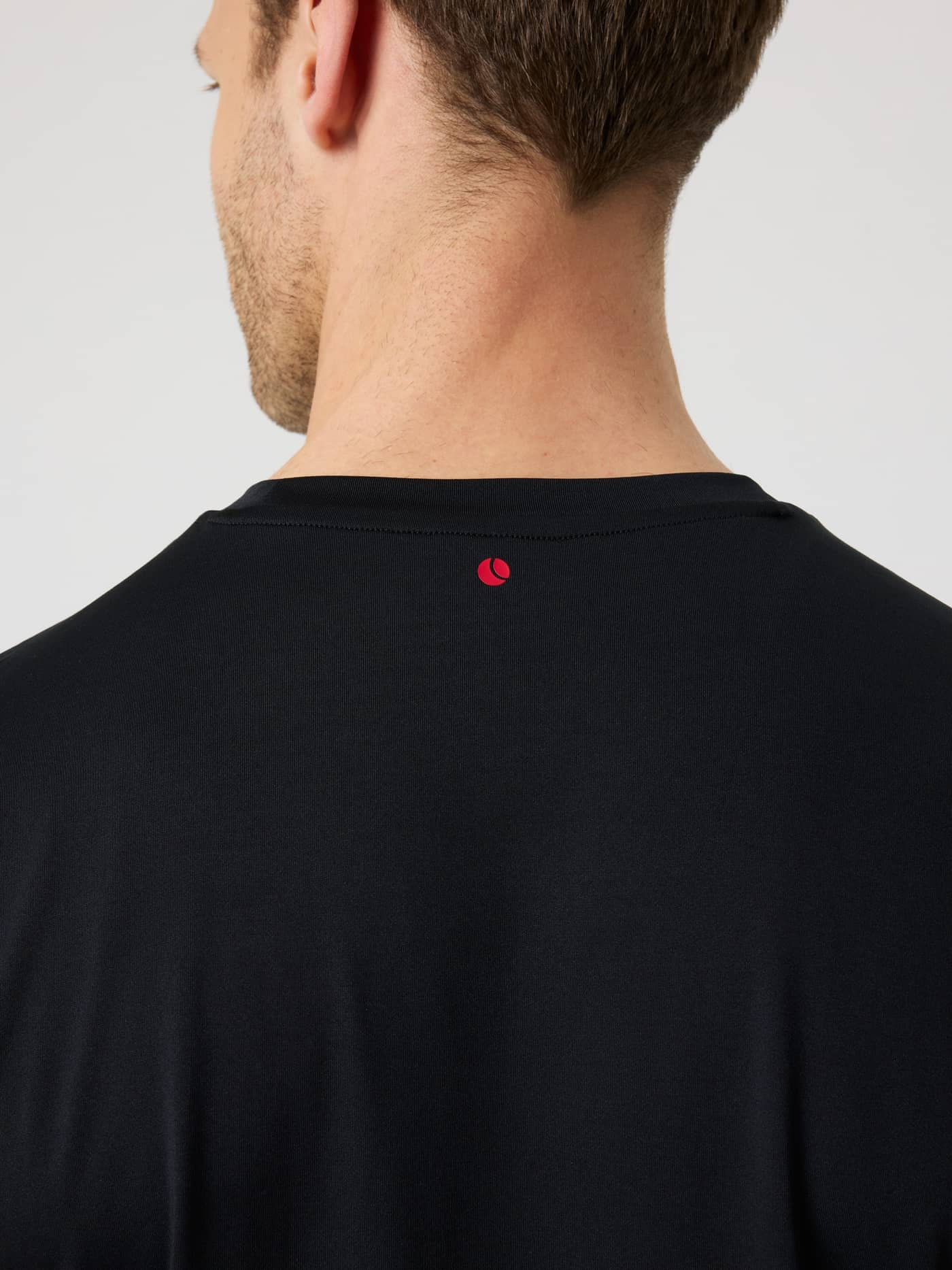 Borg T-Shirt i Black Beauty (Sort) set bagfra i nærbillede med et rødt tennisbold-logo til tennis og træning. - Image 4
