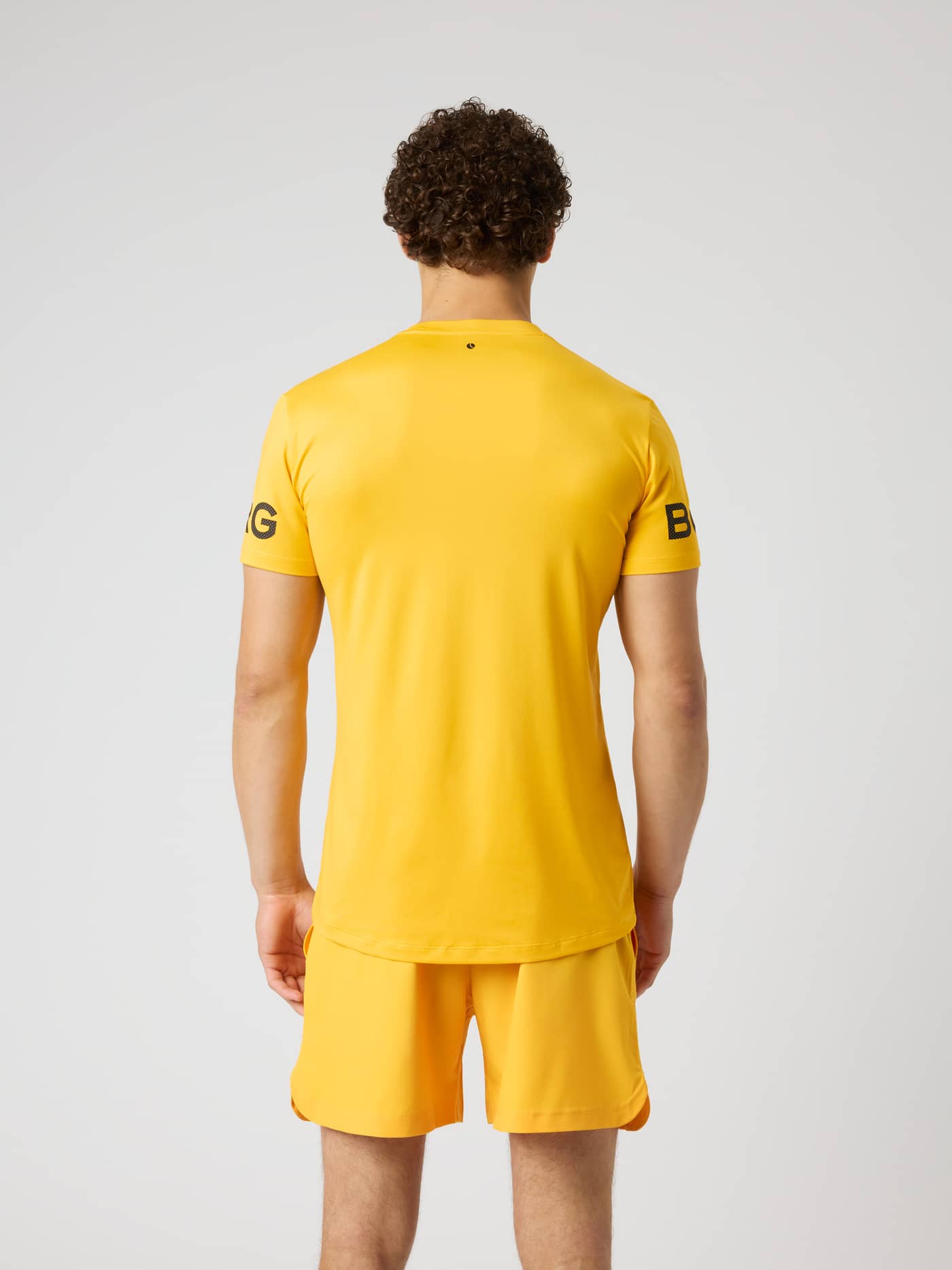 Back view of the Borg T-Shirt in Citrus (Orange) for training and tennis, featuring black sleeve logos and a longer back. - Image 2