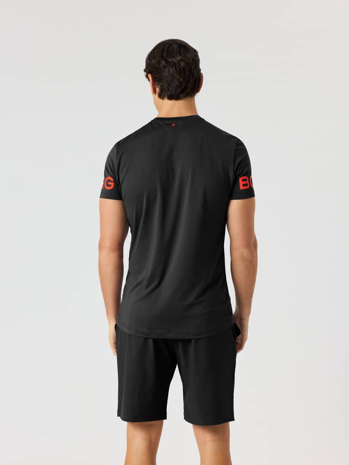 Achteraanzicht van een model in het Borg T-Shirt in Black Orange Logo (Zwart) met oranje mouwlogo's voor training. - Image 3