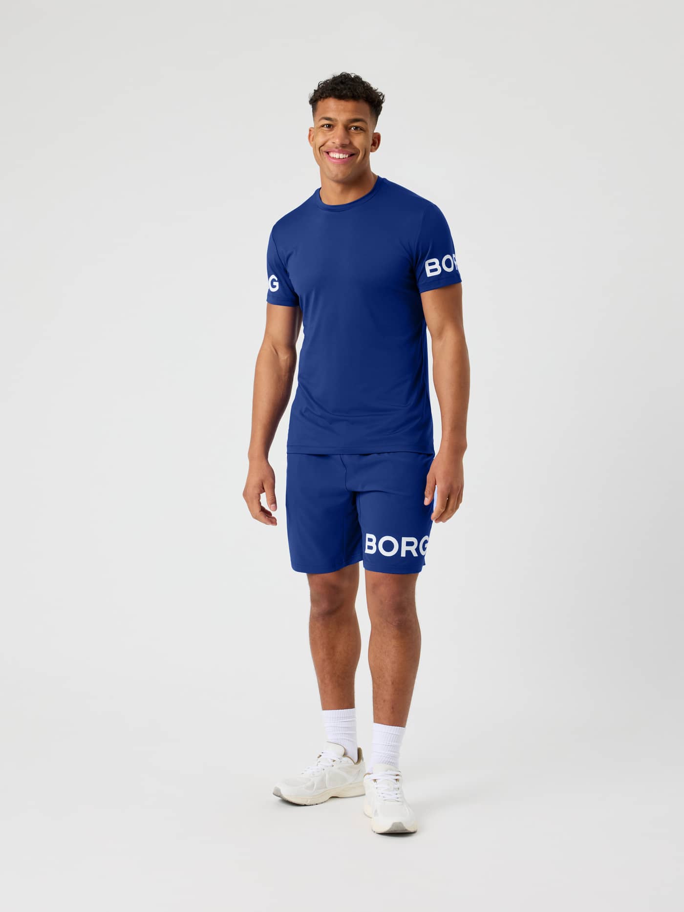 Full-body front view of a man wearing the Blue Depths (Blue) Borg T-Shirt for training, featuring white sleeve logos. - Image 3