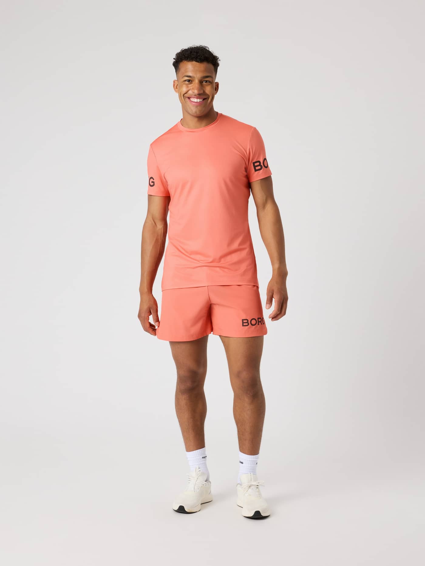 Borg T-Shirt i Coral (Orange) set forfra på en mand, en funktionel trænings-t-shirt med stil og sorte logoer. - Image 3