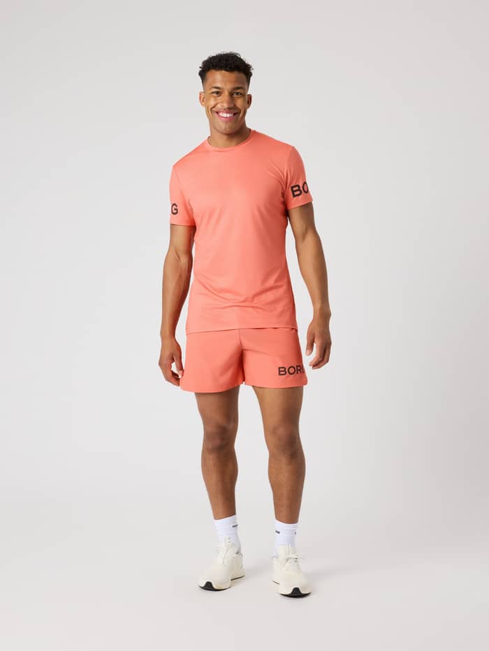 Vorderansicht eines Mannes im Borg T-Shirt in Coral (Orange), ein funktionelles Trainingsshirt mit schwarzen Logos. - Image 3