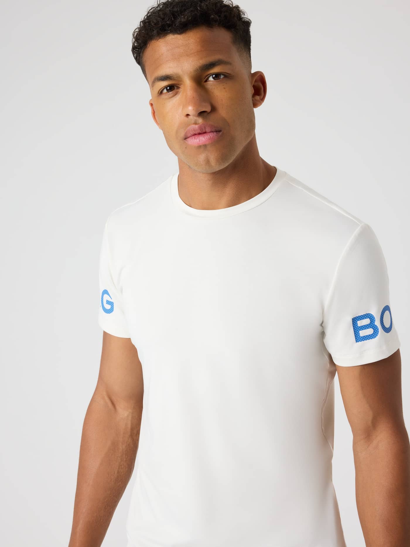 Vorderansicht eines Mannes im Borg T-Shirt in Tofu (Weiß) für das Training mit blauen Logo-Prints an den Ärmeln. - Image 5