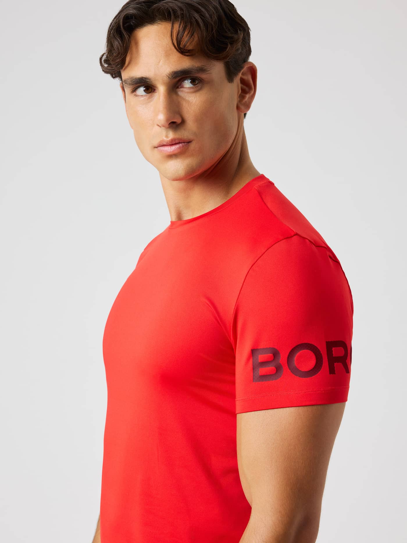 Side view of a man wearing the Borg T-Shirt in Flame Scarlet (Red) with a black logo for training and tennis. - Image 5