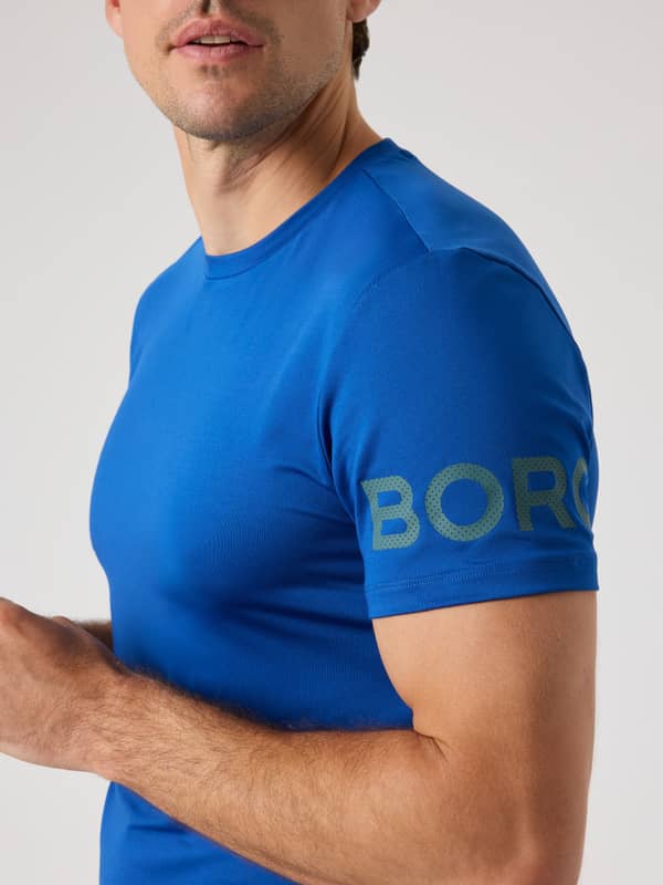 Vue de côté du Borg T-Shirt en Monaco Blue (Bleu) pour homme avec un logo vert perforé pour l'entraînement.