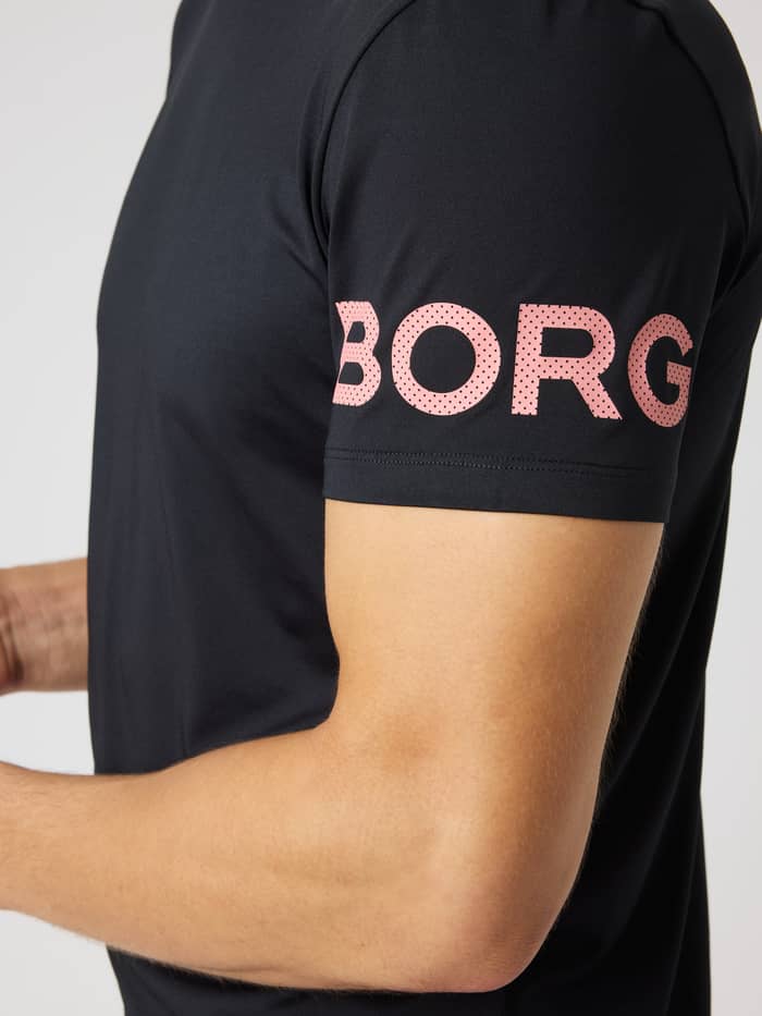 Närbild av Borg T-Shirt i Black Beauty (Svart) med rosa perforerad logotyp på ärmen för träning och tennis.