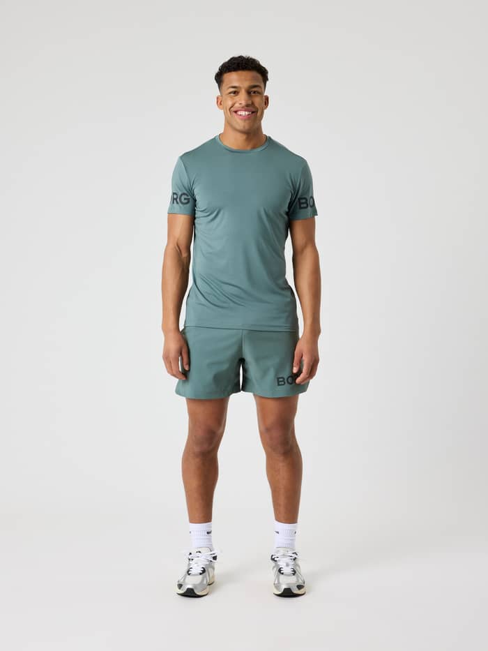 Vooraanzicht van een man in het Balsam Green (Groen) Borg T-Shirt met zwarte logo's voor tennis en training. - Image 3