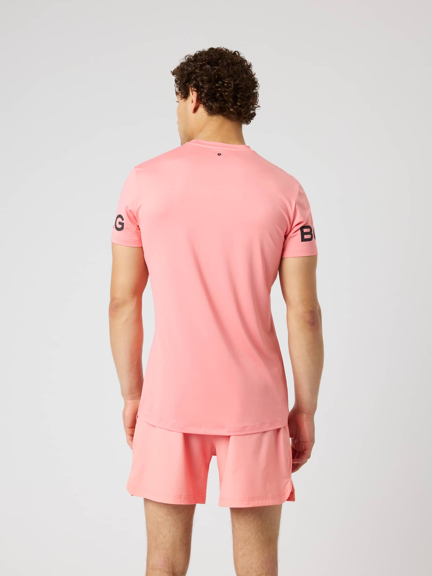 Back view of the Borg T-Shirt in Strawberry Ice (Pink) for training and tennis, with black logos and a longer back hem. - Image 3