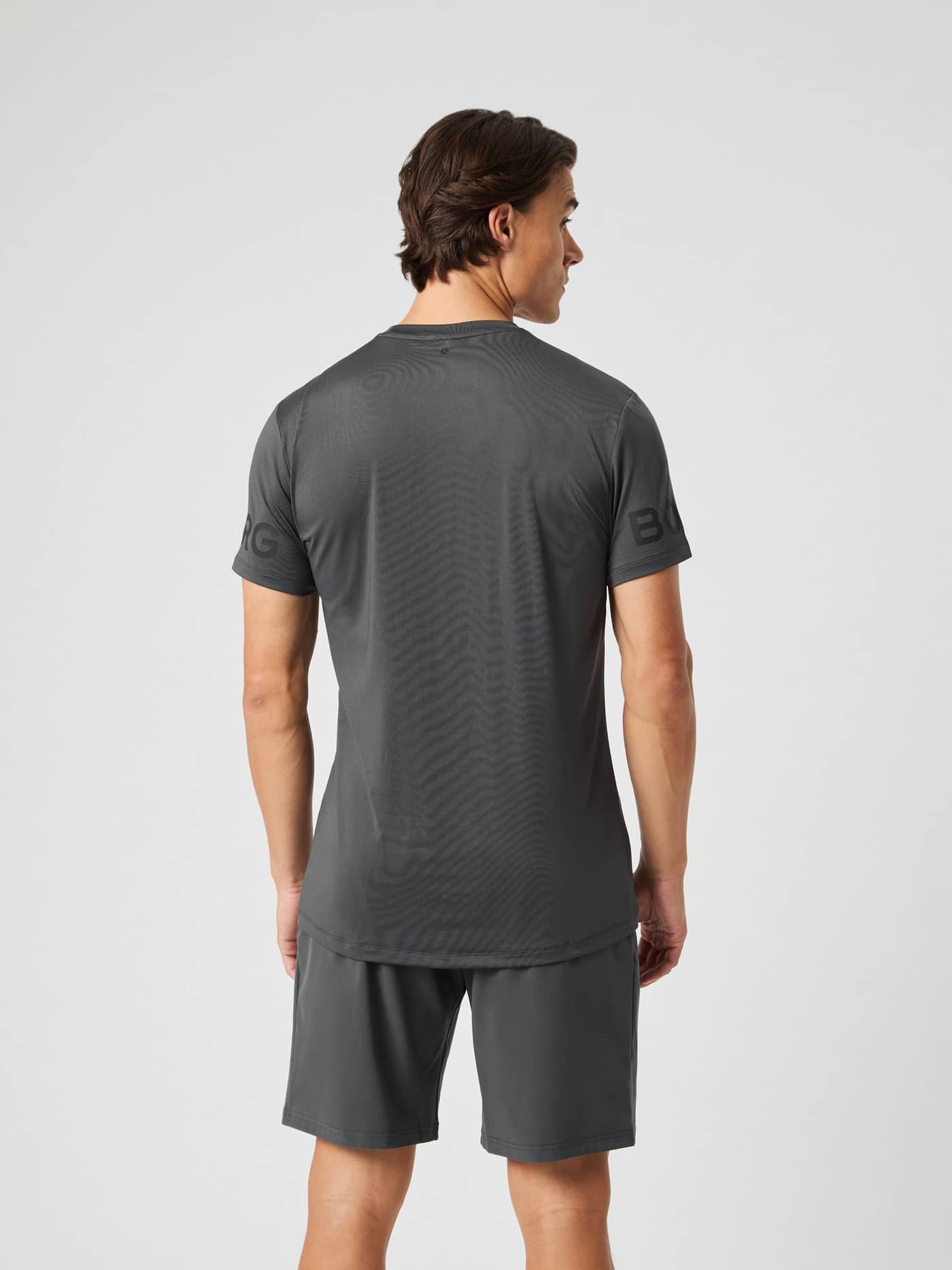 Back view of a man in the asphalt grey Borg T-shirt, featuring a longer back hem and logo on the sleeve. - Image 5