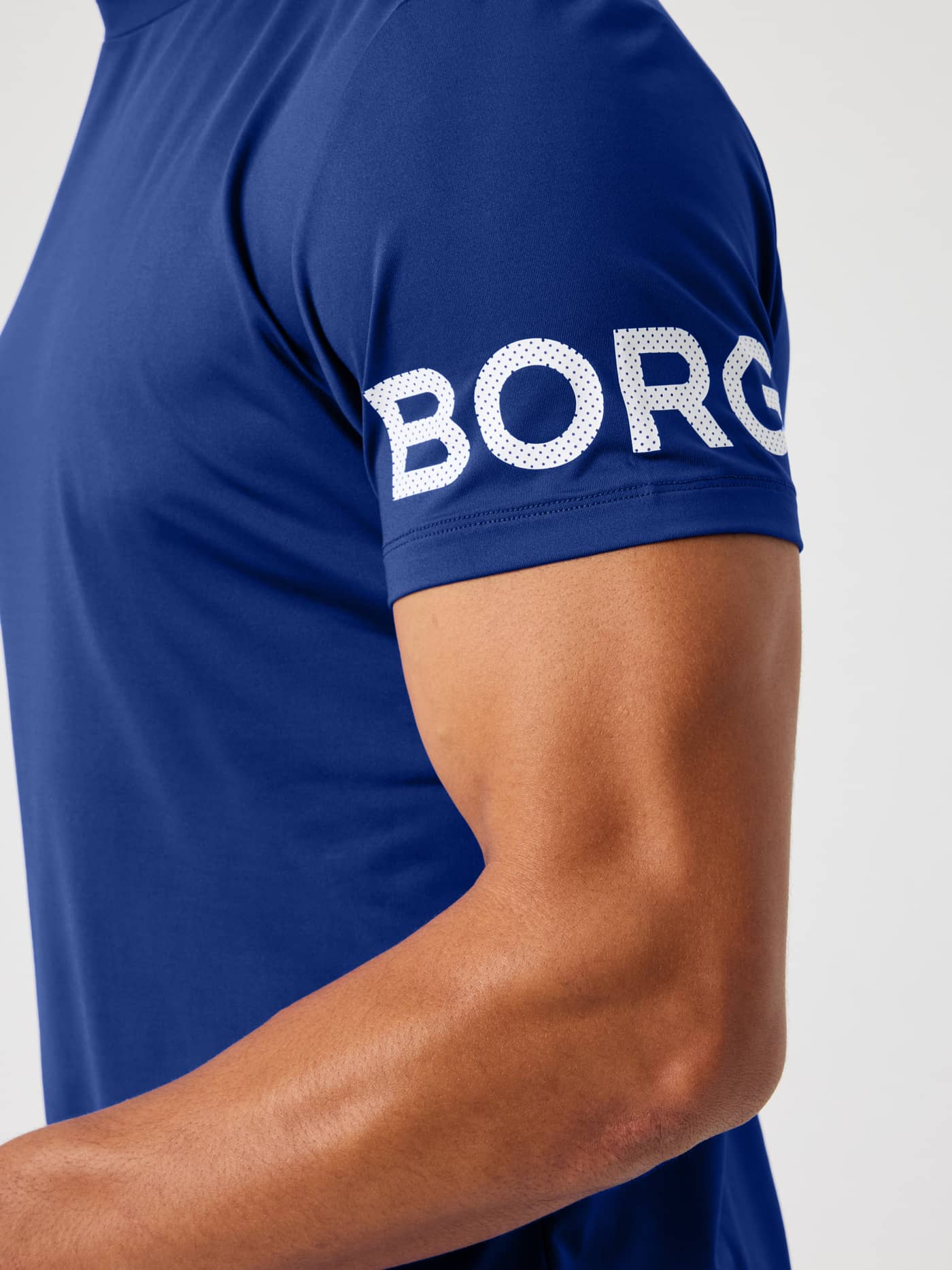 Close-up of the white perforated BORG logo on the sleeve of the Blue Depths (Blue) Borg T-Shirt for training. - Image 5
