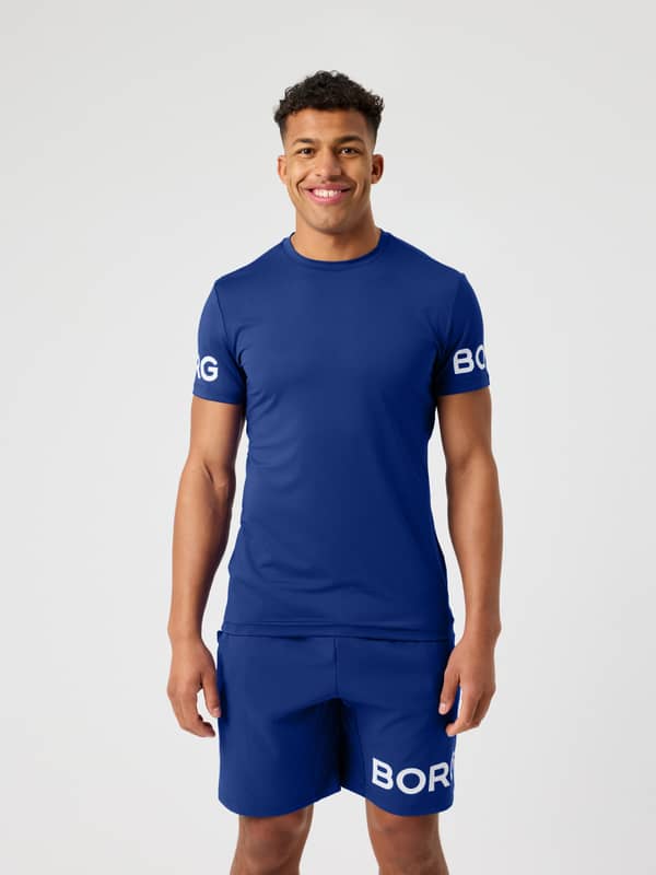 Front view of a man in the Blue Depths (Blue) Borg T-Shirt, a functional training and tennis top with white sleeve logos.