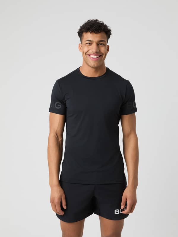 Leende modell i en Borg T-Shirt i Black Tonal Logo (Svart) av återvunnen polyester för träning och tennis.