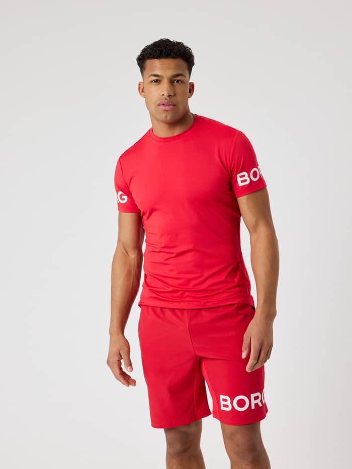 Front view of a man wearing the Björn Borg T-Shirt in Lychee (Red), a functional training top with sleeve logos.